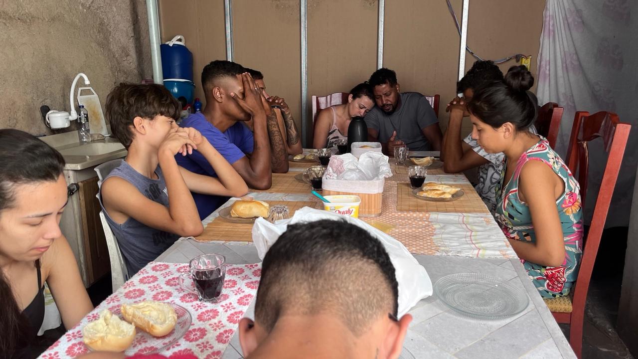 Grupo reunido à mesa para uma refeição em oração